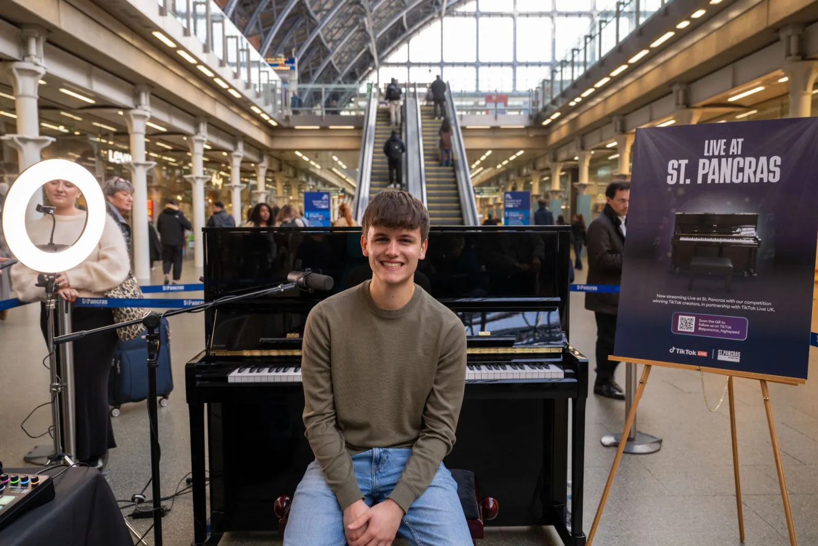 Austin sitting at the piano at St Pancras International beside a Live at St. Pancras sign